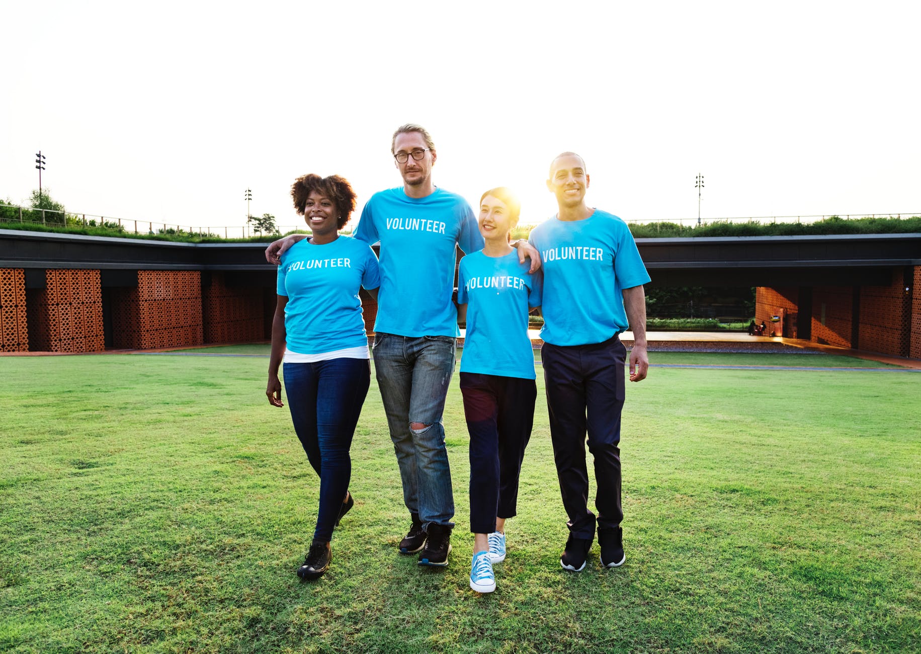 four people wearing blue crew neck shirts standing on lawn